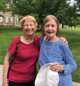 Two women pose with their arms around each other's shoulders on what looks like a college campus.